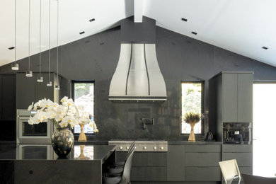 Huge trendy u-shaped eat-in kitchen photo in New York with a farmhouse sink, flat-panel cabinets, black cabinets, quartzite countertops, black backsplash, marble backsplash, paneled appliances, an island and black countertops