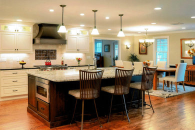 Large transitional l-shaped dark wood floor and brown floor eat-in kitchen photo in Boston with an undermount sink, raised-panel cabinets, white cabinets, granite countertops, white backsplash, ceramic backsplash, stainless steel appliances, an island and white countertops