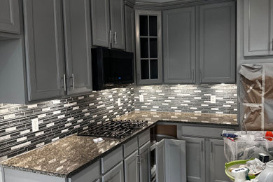 Mid-sized minimalist galley ceramic tile and white floor eat-in kitchen photo in Houston with a single-bowl sink, shaker cabinets, gray cabinets, granite countertops, gray backsplash, glass tile backsplash, stainless steel appliances, an island and black countertops