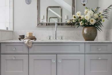 This is an example of a large eclectic ensuite bathroom in Chicago with recessed-panel cabinets, grey cabinets, marble worktops, white worktops, a single sink, a built in vanity unit, white tiles, marble tiles, a one-piece toilet, grey walls, mosaic tile flooring, a built-in sink, white floors, a hinged door, a shower bench and a double shower.