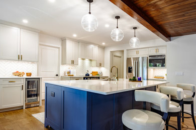 Mid-sized transitional l-shaped medium tone wood floor, brown floor and wood ceiling open concept kitchen photo in Columbus with an undermount sink, shaker cabinets, blue cabinets, quartz countertops, white backsplash, subway tile backsplash, stainless steel appliances, an island and white countertops