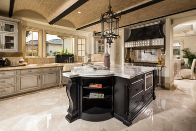 Inspiration for a large contemporary l-shaped porcelain tile enclosed kitchen remodel in Los Angeles with a farmhouse sink, shaker cabinets, distressed cabinets, marble countertops, beige backsplash, stone slab backsplash, stainless steel appliances and an island
