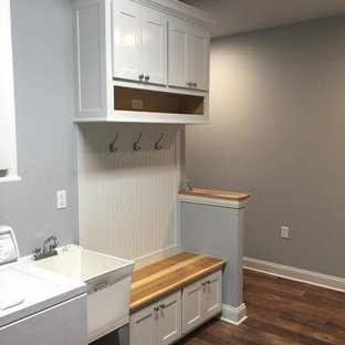 シカゴの中サイズのトラディショナルスタイルのおしゃれな家事室 (スロップシンク、シェーカースタイル扉のキャビネット、白いキャビネット、グレーの壁、無垢フローリング、左右配置の洗濯機・乾燥機、茶色い床) の写真