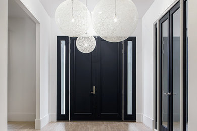 Large trendy light wood floor and brown floor entryway photo in New York with white walls and a black front door