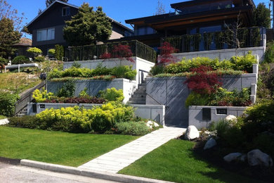 Photo of a large contemporary front yard full sun xeriscape in Vancouver with a retaining wall and concrete pavers.