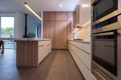 Photo of a large contemporary galley open plan kitchen in Brisbane with an undermount sink, flat-panel cabinets, white cabinets, granite benchtops, white splashback, stone slab splashback, stainless steel appliances, porcelain floors, with island and grey floor.