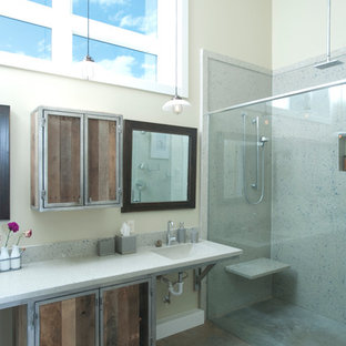 Cette image montre une grande salle de bain principale urbaine avec des portes de placard en bois brun, une douche double, un WC à poser, un carrelage gris, des carreaux de béton, un mur gris, béton au sol, un lavabo intégré et un plan de toilette en verre recyclé.