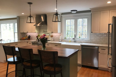 Kitchen - mid-sized farmhouse u-shaped light wood floor kitchen idea in Boston with a farmhouse sink, flat-panel cabinets, white cabinets, quartz countertops, white backsplash, porcelain backsplash, stainless steel appliances, an island and white countertops