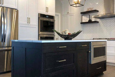 Example of a large transitional u-shaped vinyl floor and brown floor eat-in kitchen design in Omaha with an undermount sink, shaker cabinets, white cabinets, quartz countertops, white backsplash, porcelain backsplash, stainless steel appliances, an island and gray countertops