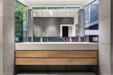 Mid-sized modern master bathroom in Melbourne with medium wood cabinets, a one-piece toilet, white tile, porcelain tile, porcelain floors, solid surface benchtops, flat-panel cabinets, grey walls, grey floor and beige benchtops.