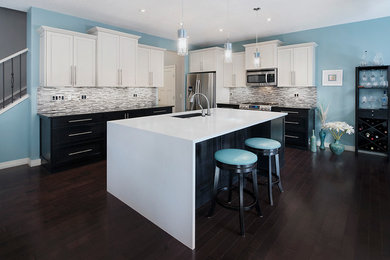 This is an example of a large contemporary single-wall eat-in kitchen in Calgary with an undermount sink, recessed-panel cabinets, white cabinets, solid surface benchtops, multi-coloured splashback, matchstick tile splashback, stainless steel appliances, dark hardwood floors and with island.