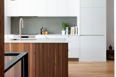 Design ideas for a mid-sized midcentury single-wall kitchen in Montreal with an undermount sink, flat-panel cabinets, white cabinets, quartz benchtops, grey splashback, engineered quartz splashback, stainless steel appliances, medium hardwood floors, with island and white benchtop.