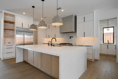 Transitional l-shaped kitchen in Dallas with an undermount sink, shaker cabinets, white cabinets, white splashback, medium hardwood floors, with island, brown floor and white benchtop.