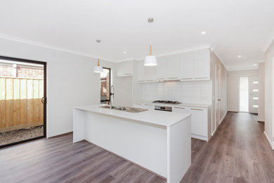 Design ideas for a modern single-wall kitchen in Melbourne with white cabinets, white splashback, subway tile splashback, white appliances, with island and white benchtop.
