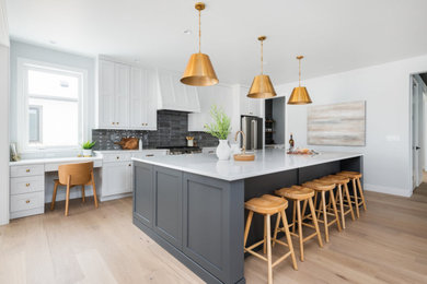 Example of a transitional galley light wood floor eat-in kitchen design in Denver with a farmhouse sink, shaker cabinets, white cabinets, quartz countertops, gray backsplash, ceramic backsplash, stainless steel appliances, an island and white countertops