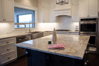 Example of a mid-sized transitional l-shaped dark wood floor and brown floor enclosed kitchen design in Portland with a farmhouse sink, shaker cabinets, white cabinets, granite countertops, white backsplash, ceramic backsplash, stainless steel appliances and an island