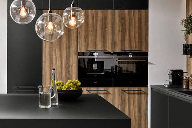 This is an example of a contemporary galley eat-in kitchen in Other with a single-bowl sink, flat-panel cabinets, black cabinets, laminate benchtops, black appliances, ceramic floors, with island, grey floor and black benchtop.