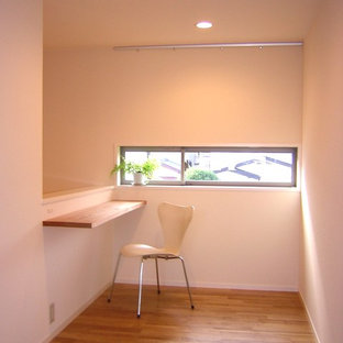 Photo of a small modern study in Other with white walls, medium hardwood flooring, no fireplace, a built-in desk and brown floors.