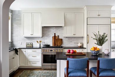Large transitional medium tone wood floor kitchen photo in DC Metro with white cabinets, white backsplash, subway tile backsplash, a peninsula and black countertops