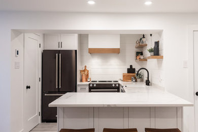 Eat-in kitchen - small country l-shaped gray floor and laminate floor eat-in kitchen idea in Montreal with a single-bowl sink, shaker cabinets, white cabinets, quartzite countertops, white backsplash, wood backsplash, black appliances, no island and white countertops