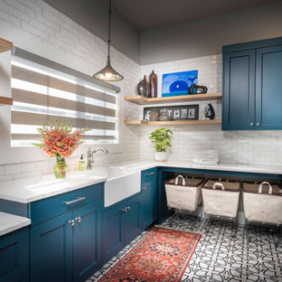 他の地域の大きいトランジショナルスタイルのおしゃれな家事室 (アンダーカウンターシンク、青いキャビネット、クオーツストーンカウンター、セラミックタイルの床、左右配置の洗濯機・乾燥機、白い床、白いキッチンカウンター、落し込みパネル扉のキャビネット、グレーの壁) の写真