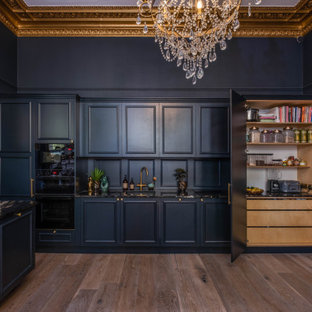 Inspiration for a large traditional single-wall eat-in kitchen in Sussex with a drop-in sink, beaded inset cabinets, blue cabinets, granite benchtops, blue splashback, timber splashback, black appliances, light hardwood floors, with island, brown floor, black benchtop and coffered.