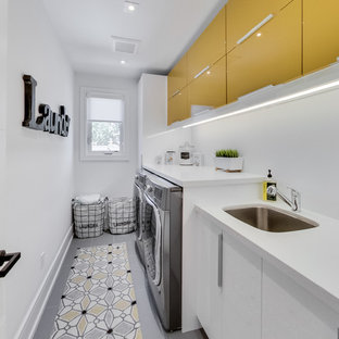 Photo of a contemporary single-wall utility room in Toronto with a submerged sink, flat-panel cabinets, yellow cabinets, white walls, a side by side washer and dryer and white worktops.