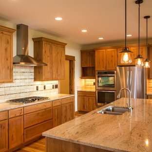 Idées déco pour une arrière-cuisine montagne en L de taille moyenne avec un évier encastré, un placard avec porte à panneau encastré, des portes de placard en bois brun, un plan de travail en granite, une crédence multicolore, une crédence en carrelage de pierre, un électroménager en acier inoxydable, un sol en bois brun et un îlot central.