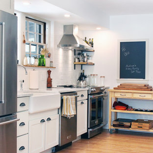Mid-sized farmhouse kitchen pantry pictures - Example of a mid-sized cottage galley medium tone wood floor kitchen pantry design in Boston with a farmhouse sink, recessed-panel cabinets, white cabinets, marble countertops, white backsplash, subway tile backsplash, stainless steel appliances, an island and white countertops