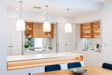 アデレードにあるコンテンポラリースタイルのおしゃれなアイランドキッチン (一体型シンク、全タイプのキャビネット扉、白いキャビネット、ガラス板のキッチンパネル) の写真