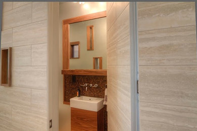 Small trendy brown tile and mosaic tile medium tone wood floor powder room photo in Portland with flat-panel cabinets, medium tone wood cabinets, a two-piece toilet, beige walls and an integrated sink
