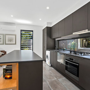 Создайте стильный интерьер: маленькая параллельная кухня-гостиная в морском стиле с накладной раковиной, плоскими фасадами, фартуком с окном, техникой из нержавеющей стали, островом, черной столешницей, серыми фасадами, столешницей из кварцевого композита, серым фартуком, полом из керамической плитки и бежевым полом - последний тренд