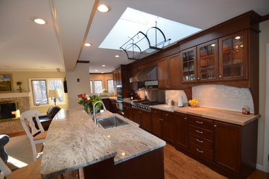Inspiration for a mid-sized timeless u-shaped medium tone wood floor and brown floor eat-in kitchen remodel in Other with an undermount sink, recessed-panel cabinets, dark wood cabinets, granite countertops, white backsplash, porcelain backsplash, stainless steel appliances, an island and multicolored countertops