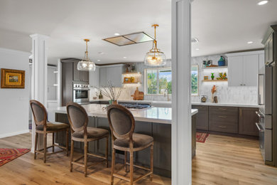 Example of a large classic vinyl floor and brown floor kitchen design in Orange County with a farmhouse sink, shaker cabinets, gray cabinets, quartzite countertops, white backsplash, marble backsplash, stainless steel appliances, an island and white countertops