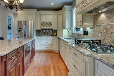 Example of a large classic l-shaped medium tone wood floor and brown floor eat-in kitchen design in Raleigh with an undermount sink, raised-panel cabinets, beige cabinets, granite countertops, beige backsplash, stone slab backsplash, stainless steel appliances, an island and beige countertops