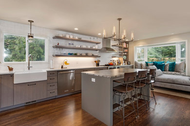 Photo of a mid-sized transitional l-shaped open plan kitchen in Seattle with a farmhouse sink, flat-panel cabinets, grey cabinets, quartzite benchtops, white splashback, subway tile splashback, stainless steel appliances, dark hardwood floors, with island and brown floor.