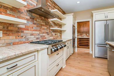 Large transitional u-shaped light wood floor kitchen photo in Boise with shaker cabinets, white cabinets, granite countertops, multicolored backsplash, stainless steel appliances and an island