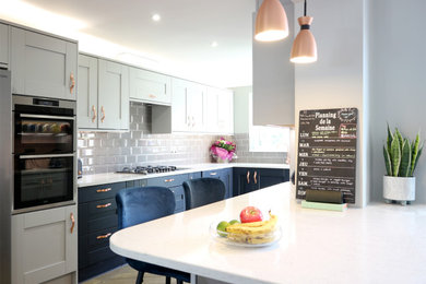 This is an example of a large modern u-shaped kitchen/diner in Hertfordshire with a belfast sink, shaker cabinets, grey cabinets, quartz worktops, grey splashback, metro tiled splashback, integrated appliances, vinyl flooring, a breakfast bar, brown floors, white worktops and feature lighting.