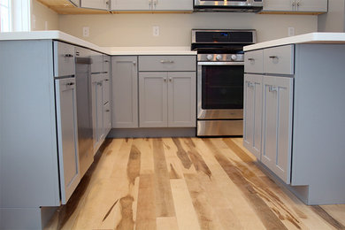 Eat-in kitchen - modern l-shaped light wood floor eat-in kitchen idea in Burlington with an undermount sink, shaker cabinets, gray cabinets, solid surface countertops, white backsplash, stainless steel appliances and an island