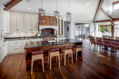 Mid-sized mountain style l-shaped dark wood floor and brown floor eat-in kitchen photo in Other with an undermount sink, recessed-panel cabinets, white cabinets, granite countertops, black backsplash, stone slab backsplash, paneled appliances and an island