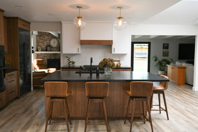 Kitchen - large 1950s vinyl floor and beige floor kitchen idea in San Diego with an undermount sink, flat-panel cabinets, brown cabinets, granite countertops, white backsplash, marble backsplash, black appliances, an island and black countertops