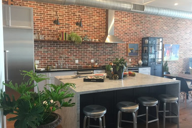 Example of a mid-sized urban l-shaped medium tone wood floor and brown floor open concept kitchen design in Los Angeles with an undermount sink, recessed-panel cabinets, white cabinets, marble countertops, red backsplash, brick backsplash, stainless steel appliances and an island