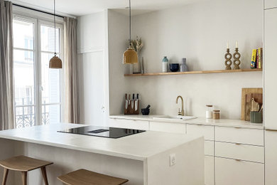 Exemple d'une cuisine ouverte parallèle de taille moyenne avec un évier encastré, parquet clair, îlot, un sol marron, des portes de placard blanches, un plan de travail en béton, une crédence blanche et un plan de travail blanc.