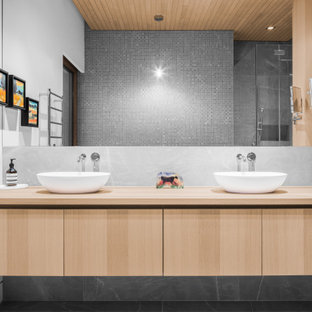 Mid-sized country master bathroom in Montreal with flat-panel cabinets, light wood cabinets, gray tile, mosaic tile, a vessel sink, wood benchtops, grey floor, a double vanity, a floating vanity and timber.