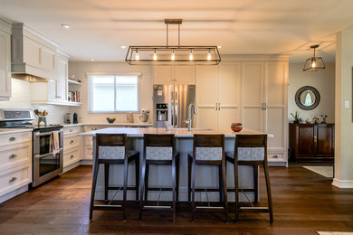 This is an example of a large transitional u-shaped eat-in kitchen in Toronto with an undermount sink, recessed-panel cabinets, white cabinets, white splashback, stainless steel appliances, medium hardwood floors, with island and brown floor.
