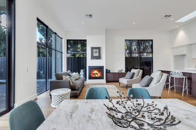 This is an example of a large contemporary family room in Adelaide with white walls, medium hardwood floors, a standard fireplace, a plaster fireplace surround and brown floor.