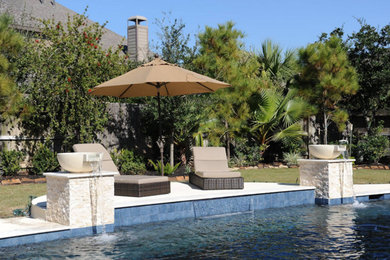 This is an example of a large contemporary backyard custom-shaped natural pool in Houston with a water feature and natural stone pavers.