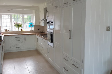 This is an example of a medium sized traditional u-shaped kitchen/diner in West Midlands with a built-in sink, shaker cabinets, white cabinets, wood worktops, white splashback, stone slab splashback, integrated appliances and no island.