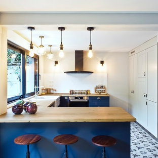 Cette photo montre une cuisine chic en U de taille moyenne avec un plan de travail en bois, une crédence blanche, un électroménager en acier inoxydable, un sol en carreaux de ciment, un évier de ferme, un placard à porte shaker, des portes de placard bleues, un sol multicolore et un plan de travail beige.