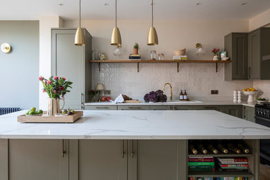 Design ideas for a large contemporary kitchen in London with a submerged sink, shaker cabinets, green cabinets, quartz worktops, white splashback, stone tiled splashback, black appliances, light hardwood flooring, an island, beige floors, white worktops and feature lighting.